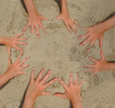 Kinderhände im Sand, die ein Mandala bilden